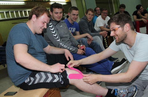 Pinkes Kinesio-Tape für das Keeper-Knie: Physiotherapeut Dennis Klück (r.) zeigt am Knie von Kreisliga-Torhüter Nico Quadflieg, wie ein Knie beklebt wird. Foto: hri